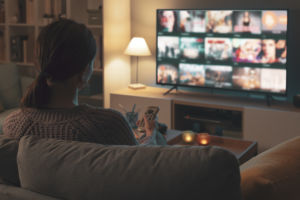 Woman relaxing on the couch, she is using the remote control and choosing a TV show or movie on the television menu