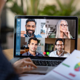 Back view of business woman talking to her colleagues about business plan in video conference. Multiethnic business team using laptop for a online meeting in video call. Group of buinessmen and businesswomen smart working from home.