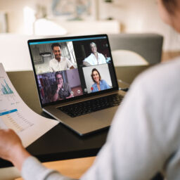 Woman holding a business report working at home having a video conference with colleagues. Over the shoulder view of a businesswoman having online business meeting from home.Businesswoman having online business meeting from home