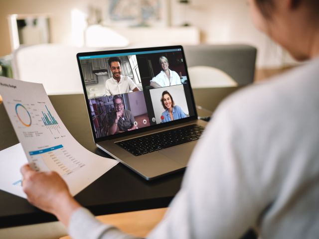 Woman holding a business report working at home having a video conference with colleagues. Over the shoulder view of a businesswoman having online business meeting from home.Businesswoman having online business meeting from home