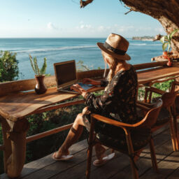 Freelance concept. Pretty young woman using laptop in cafe on tropical beach in outdoor cafe terrace with sea view. Work and travel