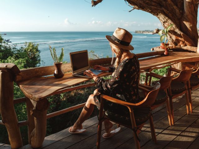 Freelance concept. Pretty young woman using laptop in cafe on tropical beach in outdoor cafe terrace with sea view. Work and travel. Freelance concept. Pretty young woman using laptop in cafe on tr