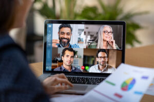 Smart working and video conference. Back view of business woman talking to her colleagues about business plan in video conference. Multiethnic business team using laptop for a online meeting in video call. Group of buinessmen and businesswomen smart working from home.