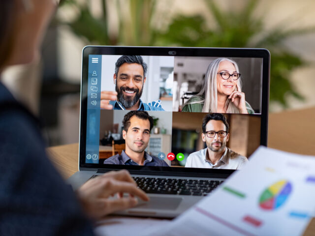 Smart working and video conference. Back view of business woman talking to her colleagues about business plan in video conference. Multiethnic business team using laptop for a online meeting in video call. Group of buinessmen and businesswomen smart working from home.