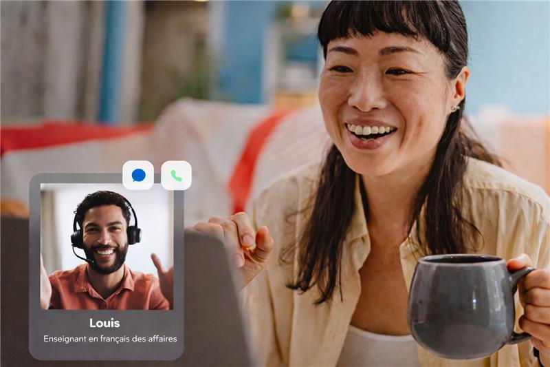Smiling woman holding a coffee mug during a one-on-one online French language lesson with her instructor Louis